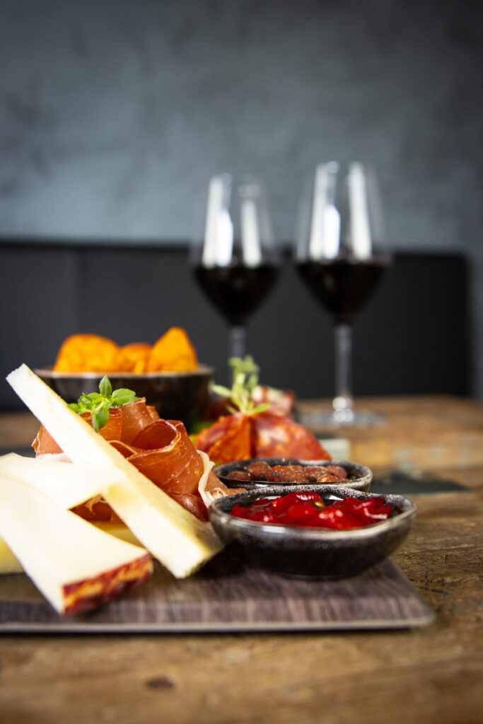 Tapasbræt med ost, skinke, chorizo og nudler serveret med to glas rødvin